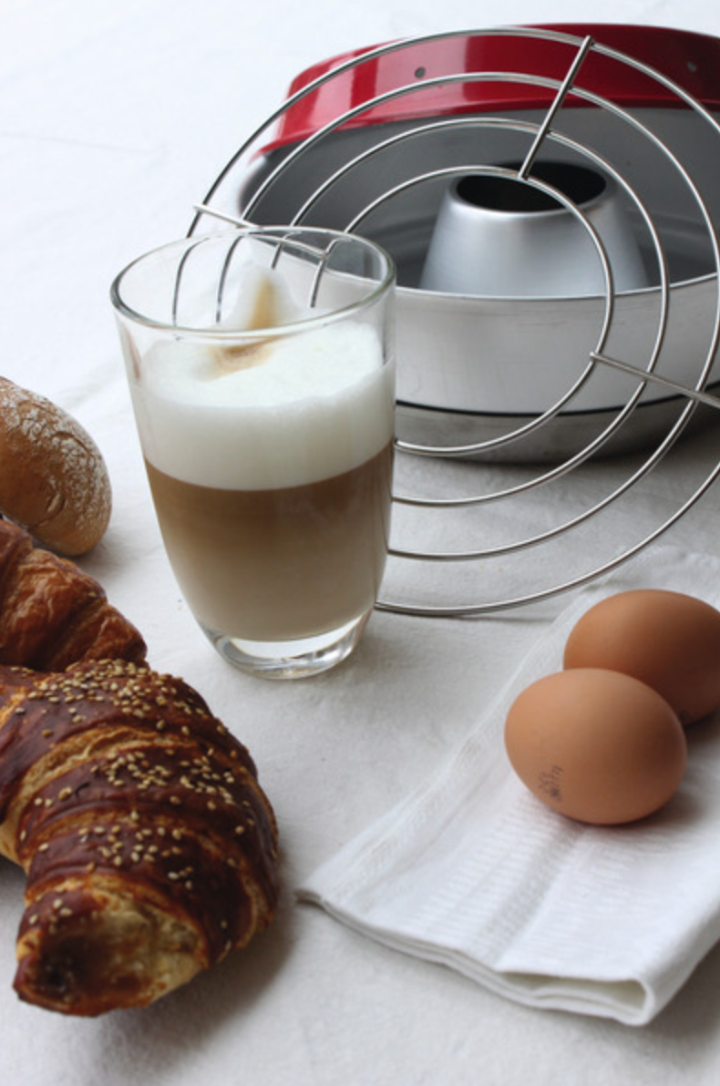 Grille de cuisson four Omnia présentée devant le moule, avec viennoiseries et boisson pour le petit-déjeuner