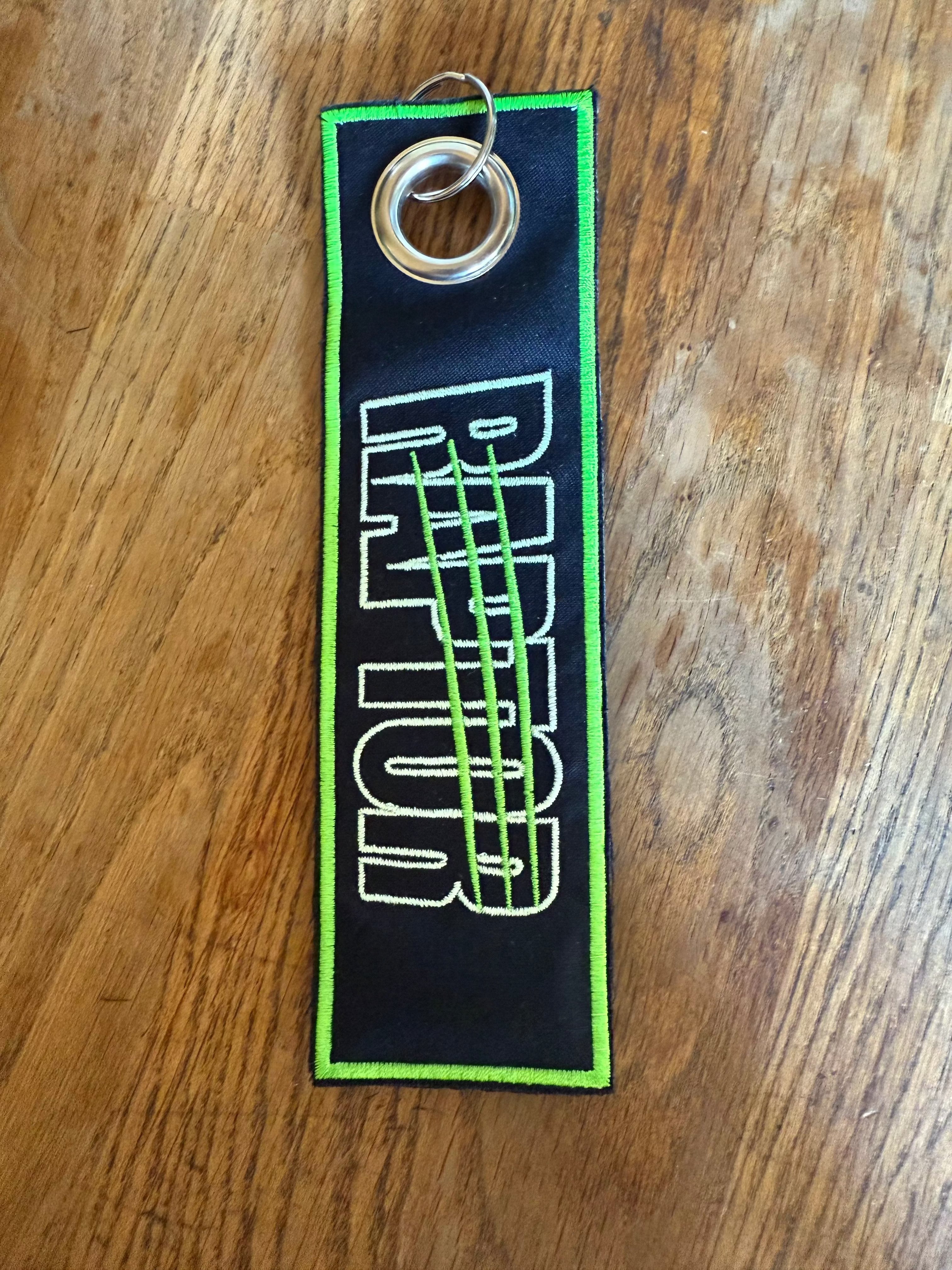 porte-clé brodé Raptor – noir lettrage bleu turquoise