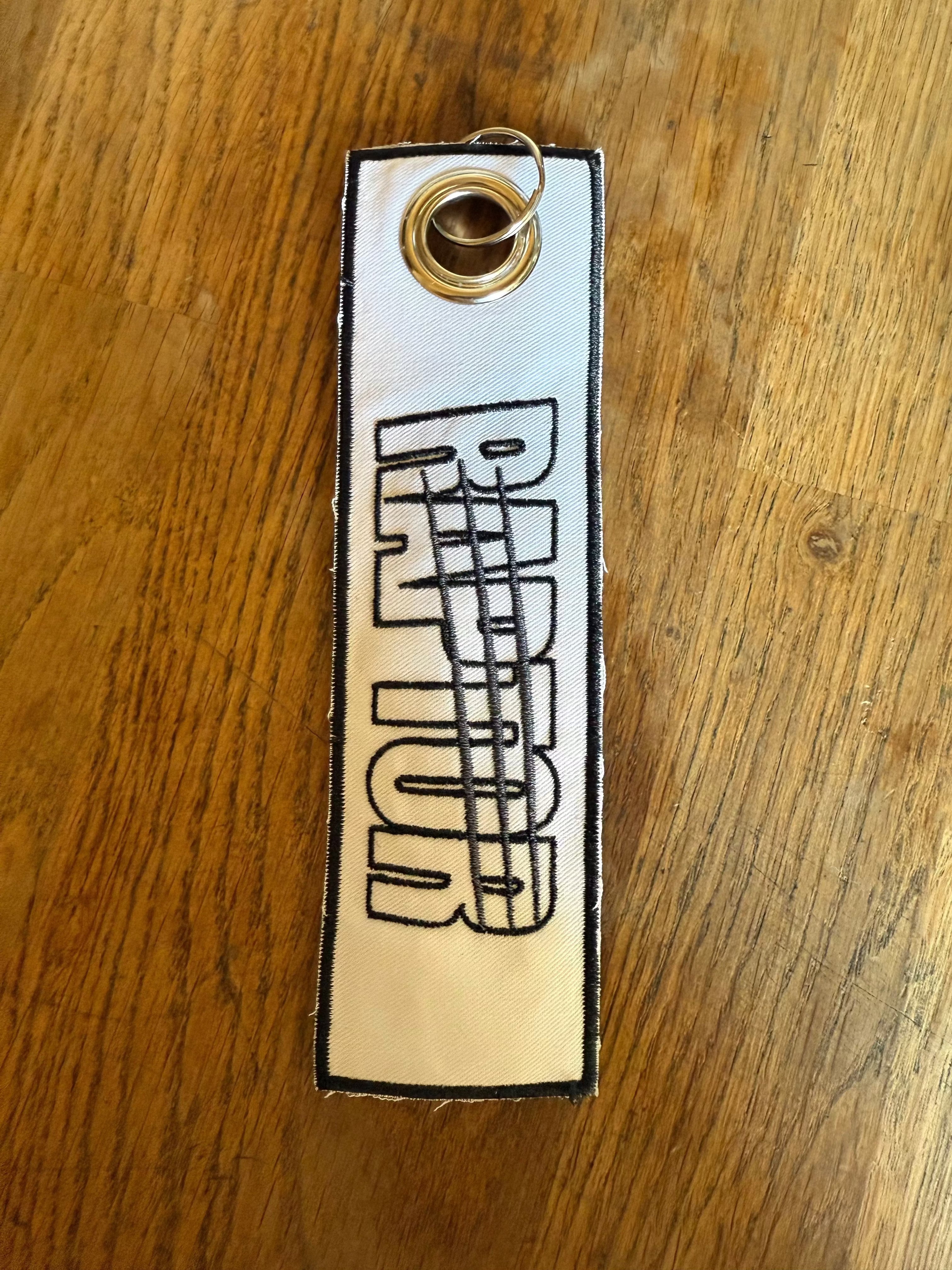 porte-clé brodé Raptor – gris lettrage doré griffes