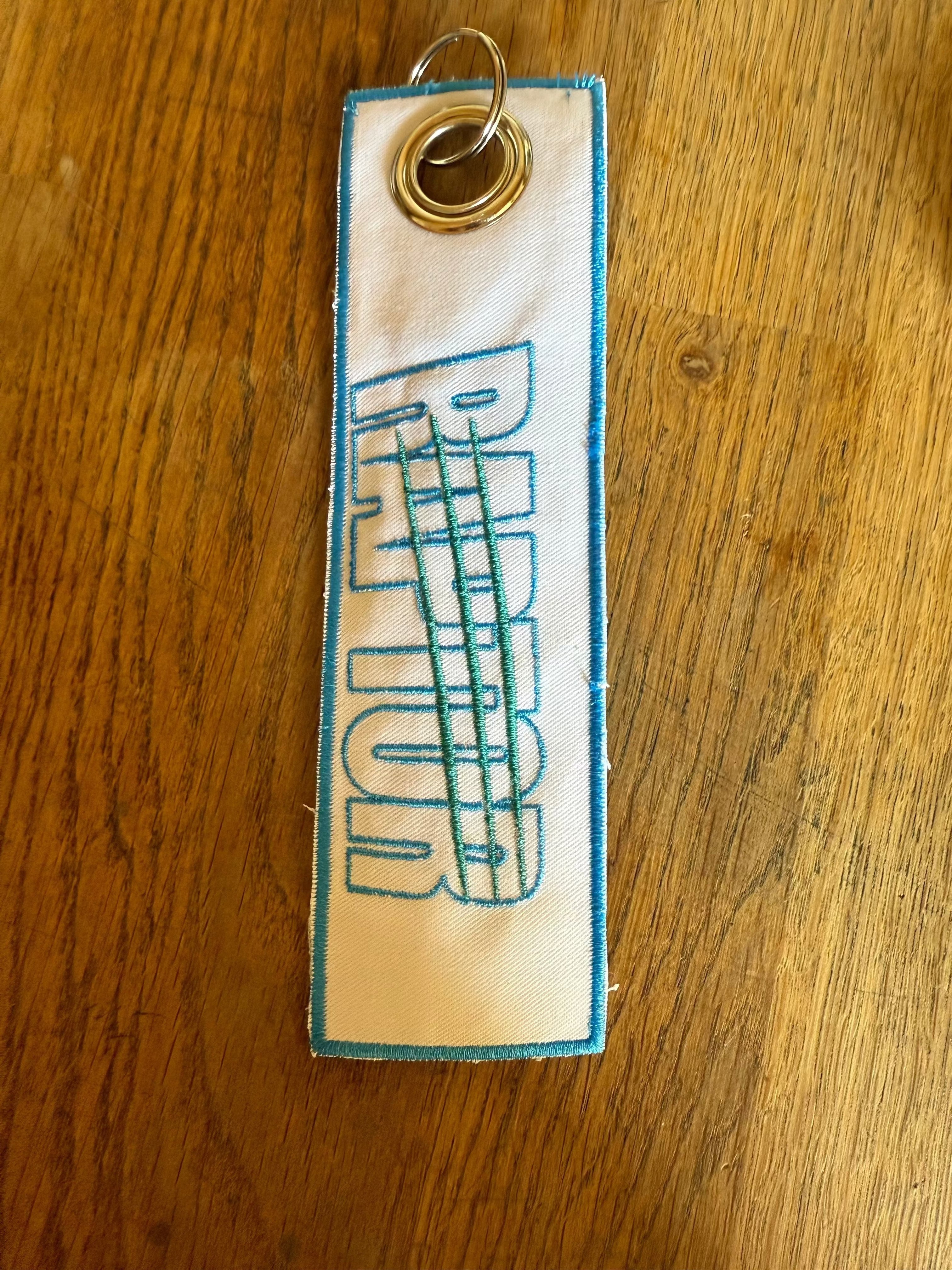 porte-clé brodé Raptor – noir lettrage bleu turquoise